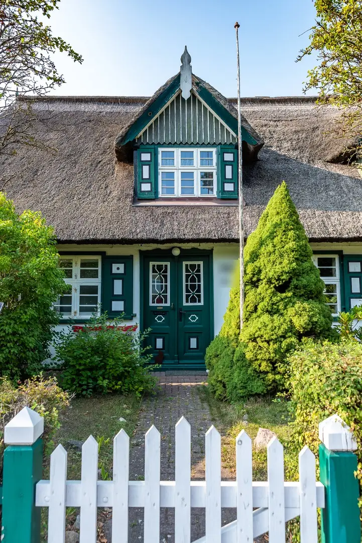 Büdnerhaus mit Reetdach und grün verschaltem Zwerchgiebel, grüne Doppeltür und Fensterläden, davor ein weißer Lattenzaun mit grünen Pfosten
