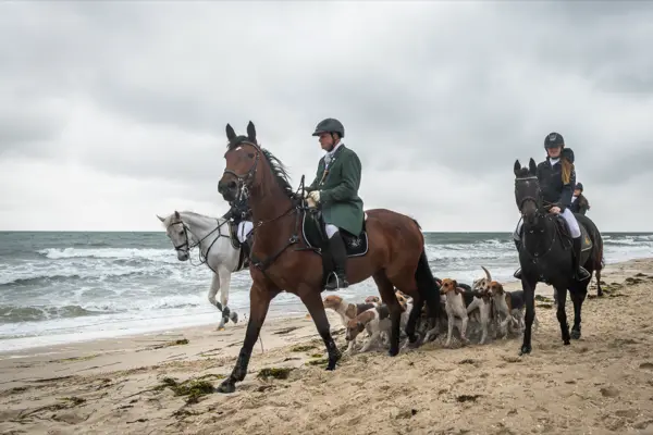 Reiter und Meute am Ostseestrand, dahinter die bewegte See