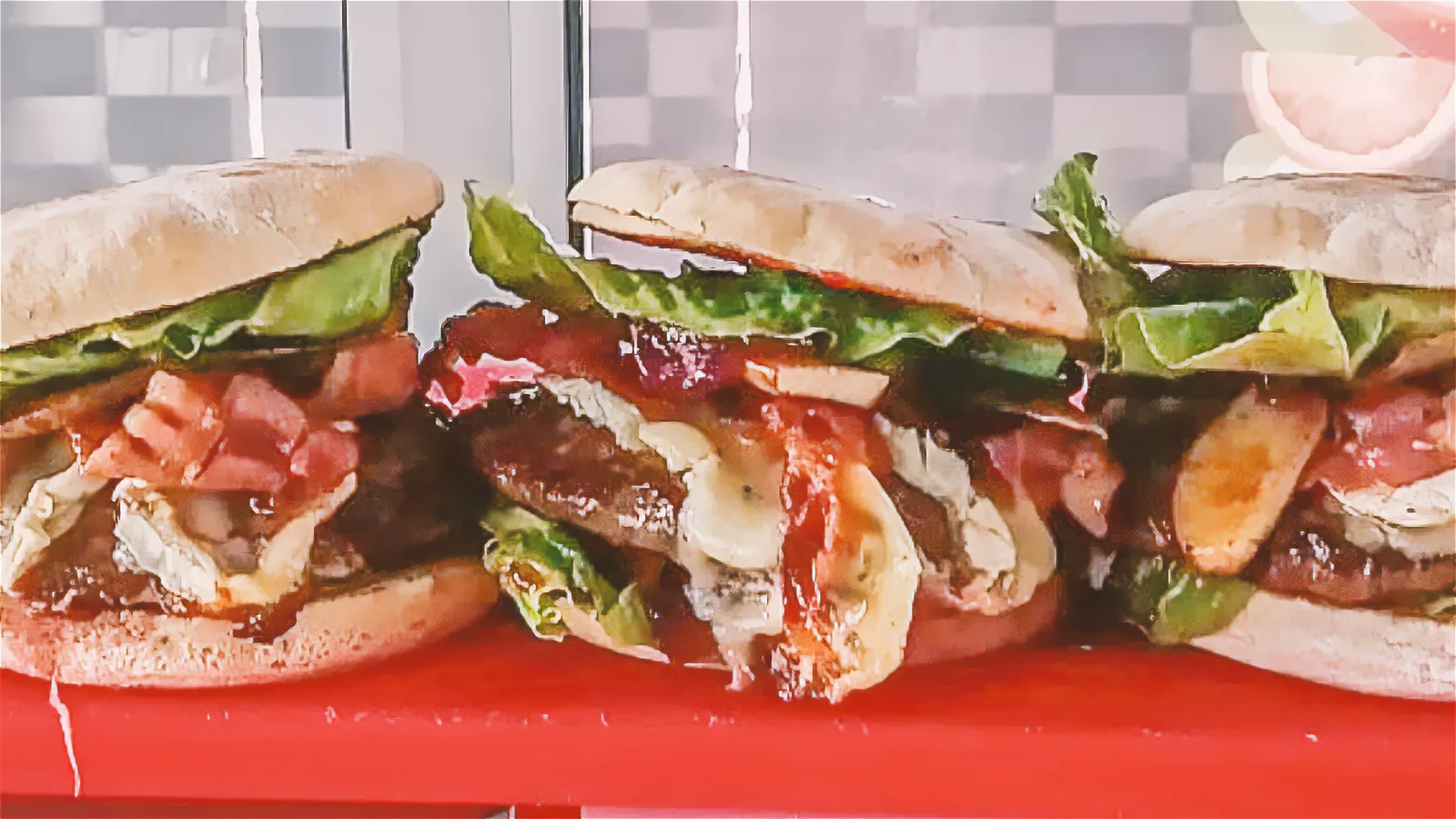 Drei Burger mit Salat, Tomate und Pilzen nebeneinander auf einer roten Theke