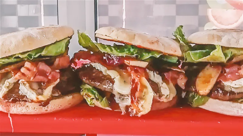 Drei Burger mit Salat, Tomate und Pilzen nebeneinander auf einer roten Theke