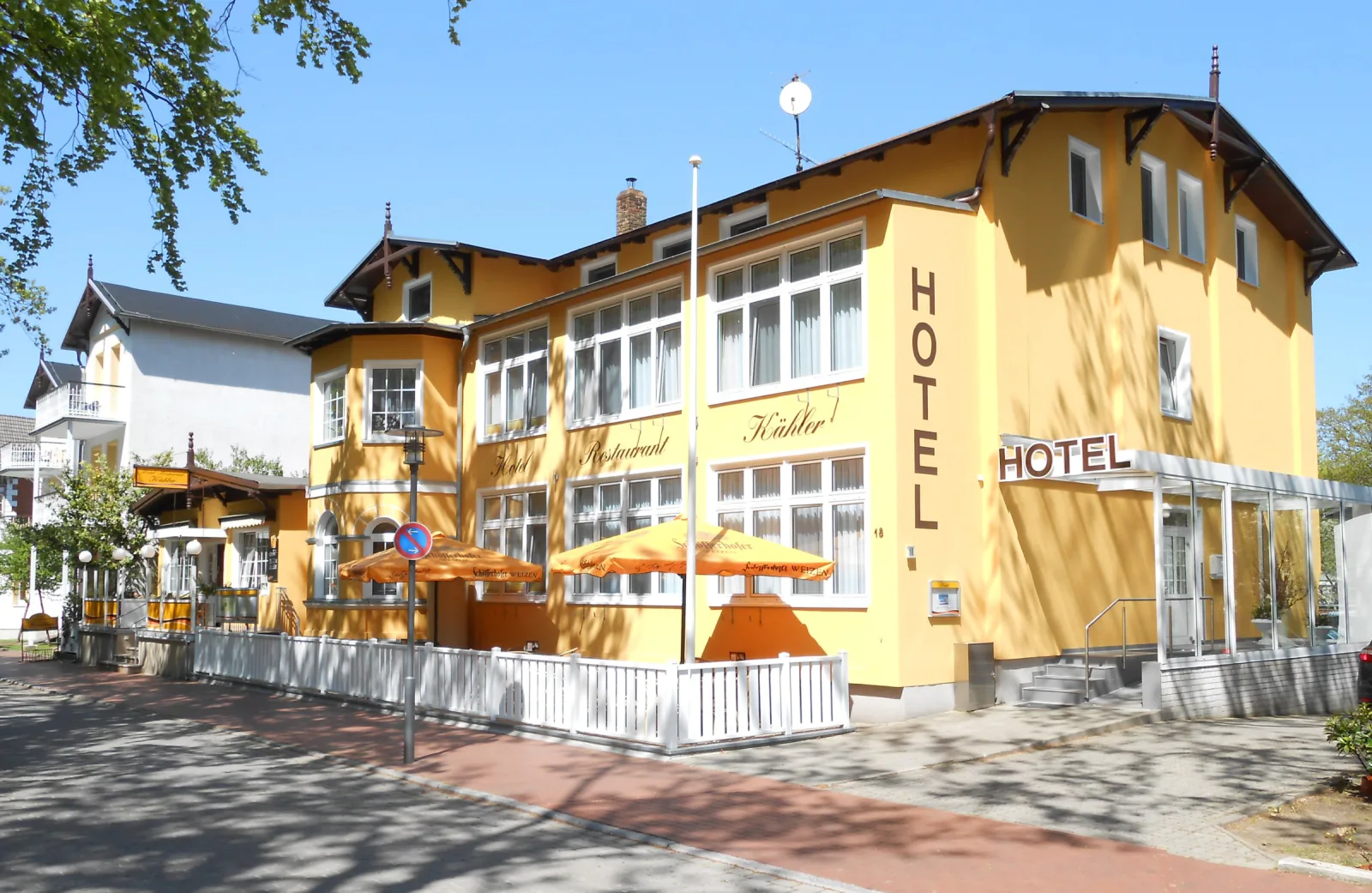 Hotel und Restaurant Kähler in Graal-Müritz: gelbe Bäderarchitektur-Villa mit Terrasse, weißem Zaun und Sonnenschirmen